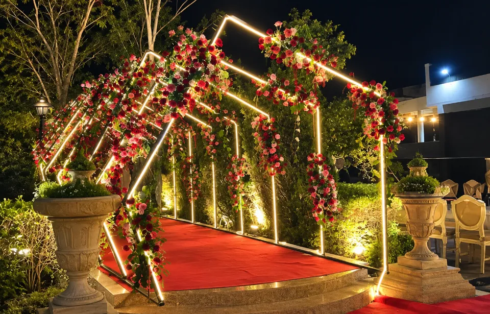 An illuminated floral tunnel of red and pink roses over a red carpet, built by Bluebird Events for a wedding entry