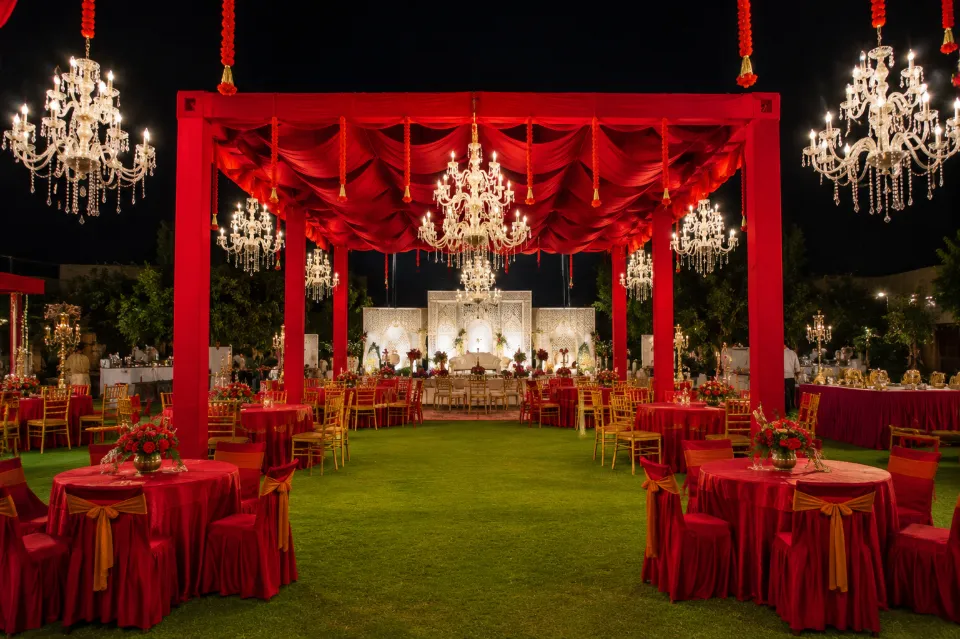 Red-draped dining tables and crystal chandeliers on a lawn at night, decorated by Bluebird Events